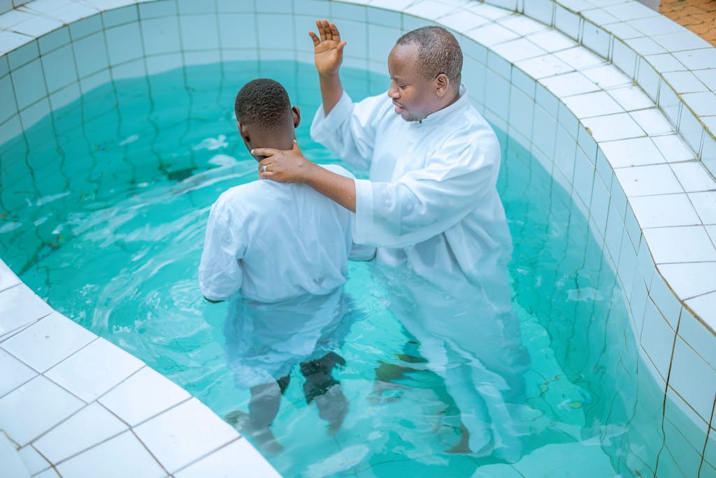 A priest performs a baptism in a clear blue pool, emphasizing faith and tradition.
