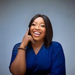 Confident woman with long black hair posing in a vibrant blue dress, smiling joyfully.