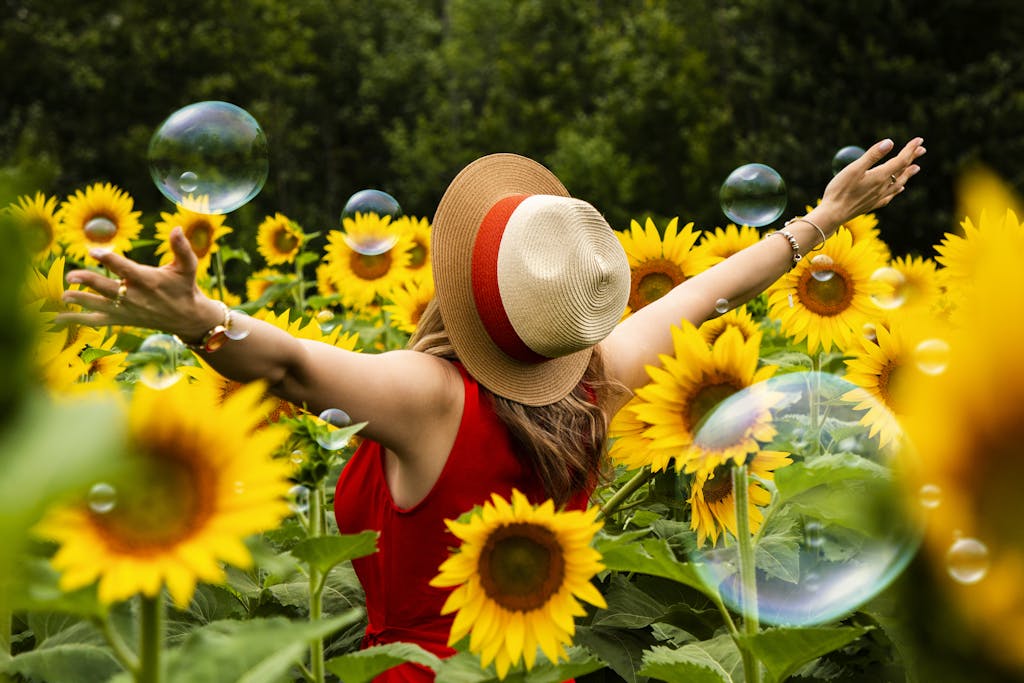 Woman enjoying a sunny day in a vibrant sunflower field with floating soap bubbles in Hamilton, Canada.